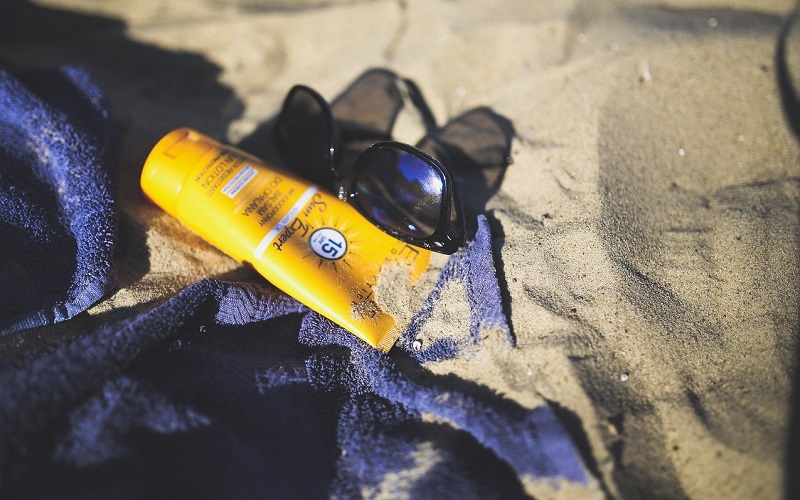crema solare, occhiali da sole e asciugamano sulla sabbia